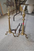 Front view of both brass andirons showing full height, bases, and rear iron supports