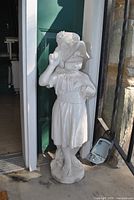 Full view of off-white concrete girl statue standing on base