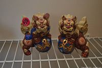 Pair of red, blue and gold ceramic foo dog statues on wire shelf
