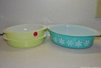 Two pistachio round dishes nested together beside turquoise snowflake oval casserole, showing exterior colors, interiors and handles