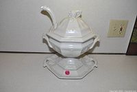 White porcelain soup tureen with lid, ladle and underplate displayed on countertop
