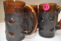 Close-up of amber glass mug with black metal sleeve showing geometric cut-outs and sticker 81