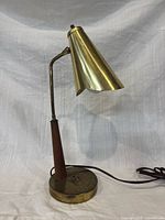 full view of lamp lit positioning showing brass cone shade, wood stem and base
