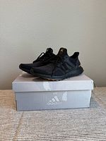 Side view of pair of black Ultraboost sneakers on original grey Adidas box