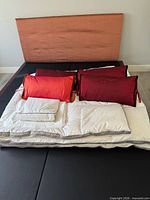 Mahogany bed frame with headboard and bedding items stacked on platform: pillows, comforter, sheets