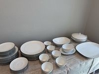 Full set laid out on table showing stacks of plates, cups, bowls, platter and covered dish