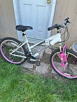 Full view of Schwinn white and pink 26-inch mountain bike against shed