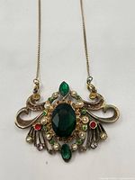 Front view of pendant showing central green glass stone, surrounding rhinestones and pearls, chain attachment