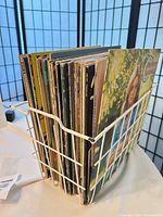Side view of upright stack of LPs in white wire rack showing jacket edges and one visible cover
