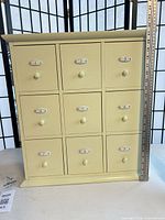 Front view of cream wooden organizer showing 9 drawers, numbered plates, knob pulls
