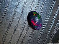 Front view of oval cabochon Ethiopian black opal showing play of colour