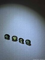 Four oval green sapphires aligned on white surface under spotlight