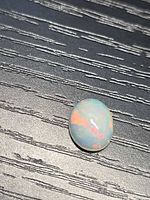 Front view of oval Ethiopian opal on dark wood surface showing play-of-colour