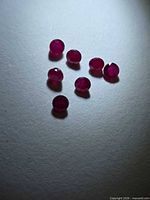 Seven small round faceted red gemstones on neutral background