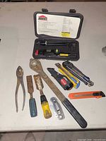 Assorted hand tools spread on table including Jobmate laser level kit, pliers, chisels, utility knives, small knife, socket adapters