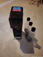 Black carbonation machine with three bottles standing beside it