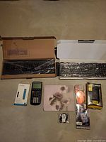 All items laid out: two boxed keyboards above, calculator, Fitbit band box, mouse pad, two phone cases, earbud tips