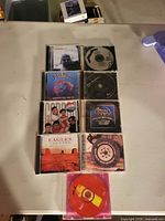 Stacked view of 9 jewel-cased CDs and one loose disc showing front artwork