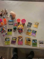 Lot overview with Pokémon cards, Play-Doh tubs, Little People figure, capsule, wooden egg, dollhouse accessories