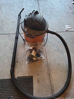 Vacuum with hose, wand and bagged attachments on floor