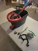 Overview of bucket, mop head in wringer, handle, brackets, hose, hardware bag