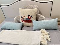 All five items on bed: grey bed-rest pillow, cream motif pillow, two light blue lumbar pillows, cream tassel throw