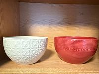 White textured ceramic bowl and red ribbed ceramic bowl on shelf