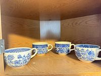 Four blue & white handled cups on cabinet shelf