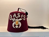 Front view of red Shriners fez showing rhinestone "OASIS" emblem and crescent/star badge