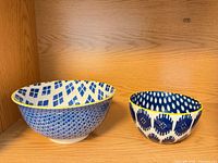 Two blue and white patterned ceramic bowls with yellow rims displayed side by side