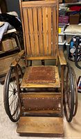 Front angle showing wood frame, leather seat, large spoked wheels, footrest