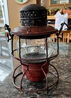 Front view of vintage railroad lantern showing wire guard, red painted body, clear glass globe, and top vent.