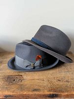 Two gray wool felt hats stacked, showing side profiles, bands and feather