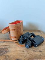 Binoculars beside open brown leather case, neck strap visible