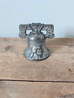 Front view showing patinated cast iron Liberty Bell figure with relief portrait and decorative yoke