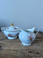 Front view of creamer and lidded sugar bowl showing floral design and gold trim