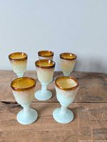 Front angled view of all six cordial glasses showing amber rims and seafoam stems
