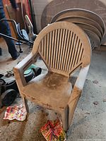 Front view of dirty light grey plastic chair with slatted back; additional stacked chairs visible behind