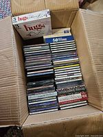 Open cardboard box containing two stacks of CDs and a 3-disc box set