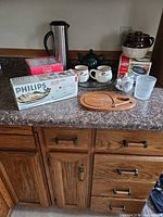 Overall countertop view showing multiple items including boxed Philips knife, Thermos, mugs, teapot, bean pot, Little Dipper