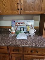 Overall lot on countertop showing boxed tray, tea sets, crystal pieces, porcelain pieces, milk frother, napkin rings