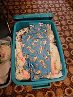 Top view of teal plastic tote filled with folded cotton and flannel fabrics, showing blue cartoon print and other light-patterned pieces