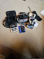 Group view of binoculars, cameras, radio, accessories on floor