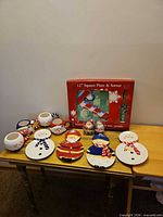 All pieces on table: square plate box, snowman mug and plate sets, Santa salt & pepper, platters