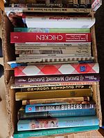 Stack of assorted cookbooks in first box showing titles like Chicken, Bread Machine Baking, Big Book of Burgers