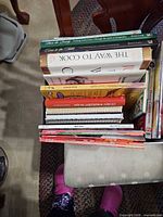Top-down view of a stack of approximately 14 cookbooks on a chair