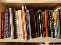 First shelf of assorted hardcover, softcover and spiral cookbooks