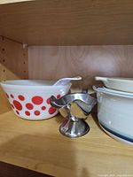 Shelf showing mixing bowl with red dots, stainless gravy boat and stoneware casserole