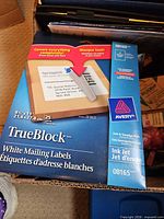 Avery TrueBlock mailing labels box and surrounding office supplies visible in storage bin
