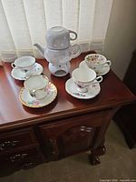 Four floral teacup and saucer sets alongside grey stackable teapot-and-cup